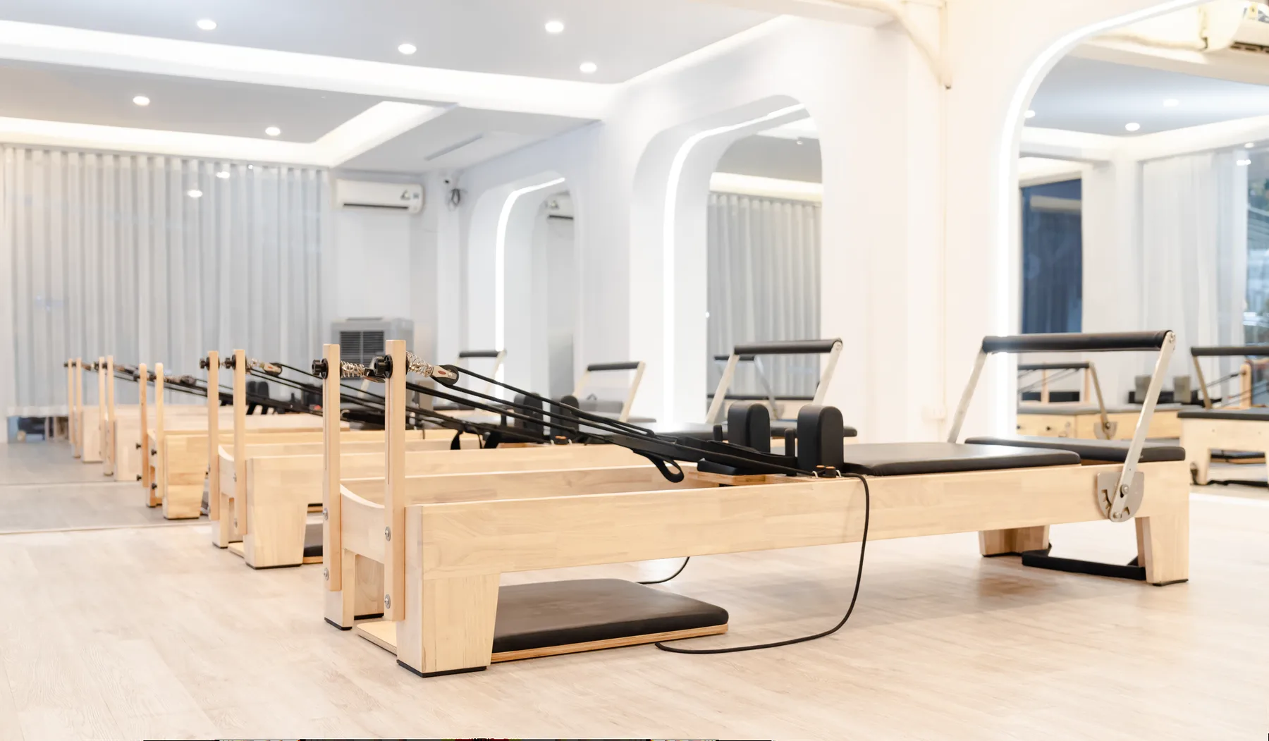 Rangée de Reformers en bois clair dans un studio de Pilates blanc